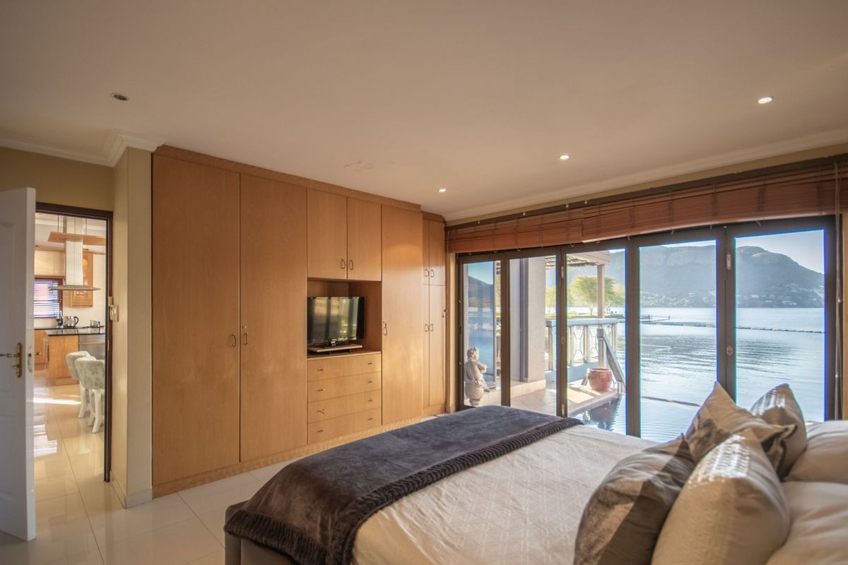 Spacious bedroom featuring extensive built-in wooden cabinetry, tiled flooring, and large sliding glass doors opening to a scenic waterfront patio.