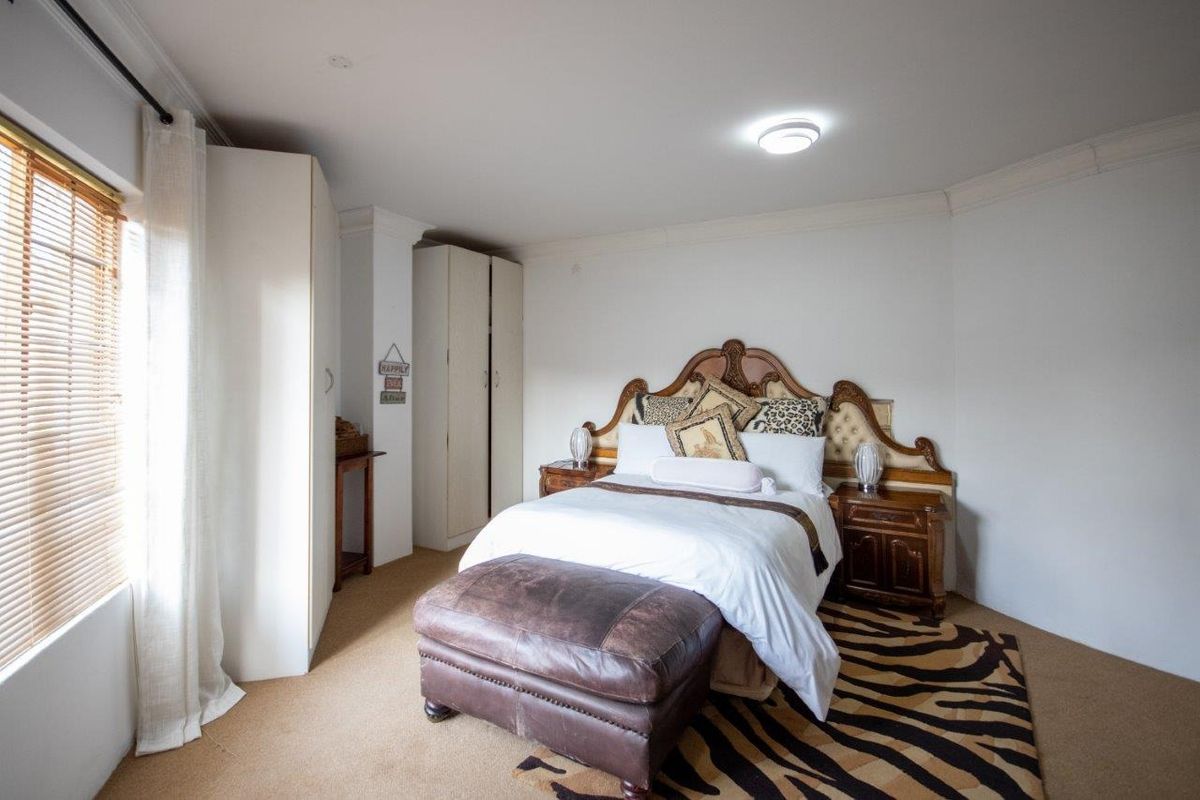 A well-lit bedroom featuring neutral carpeting, built-in storage cupboards, and venetian blinds, offering a comfortable and functional living space.
