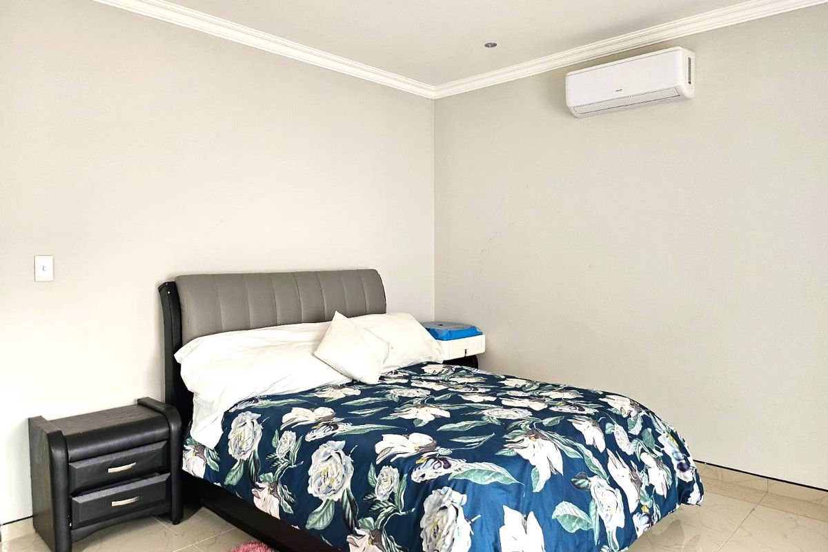 A well-maintained bedroom featuring tiled flooring, crown molding, and a wall-mounted air conditioning unit.