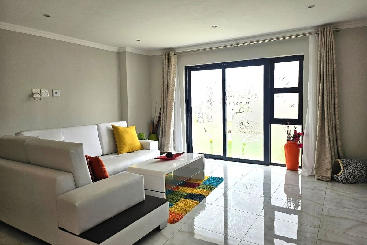 A bright living room featuring polished porcelain floor tiles, recessed ceiling lighting, and large sliding glass doors providing access to the exterior.