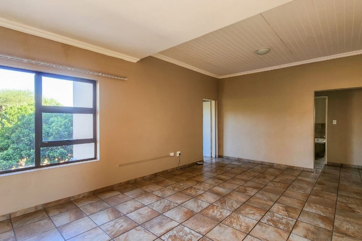 An empty living room featuring tiled flooring, neutral wall tones, and a large window providing natural light and garden views.