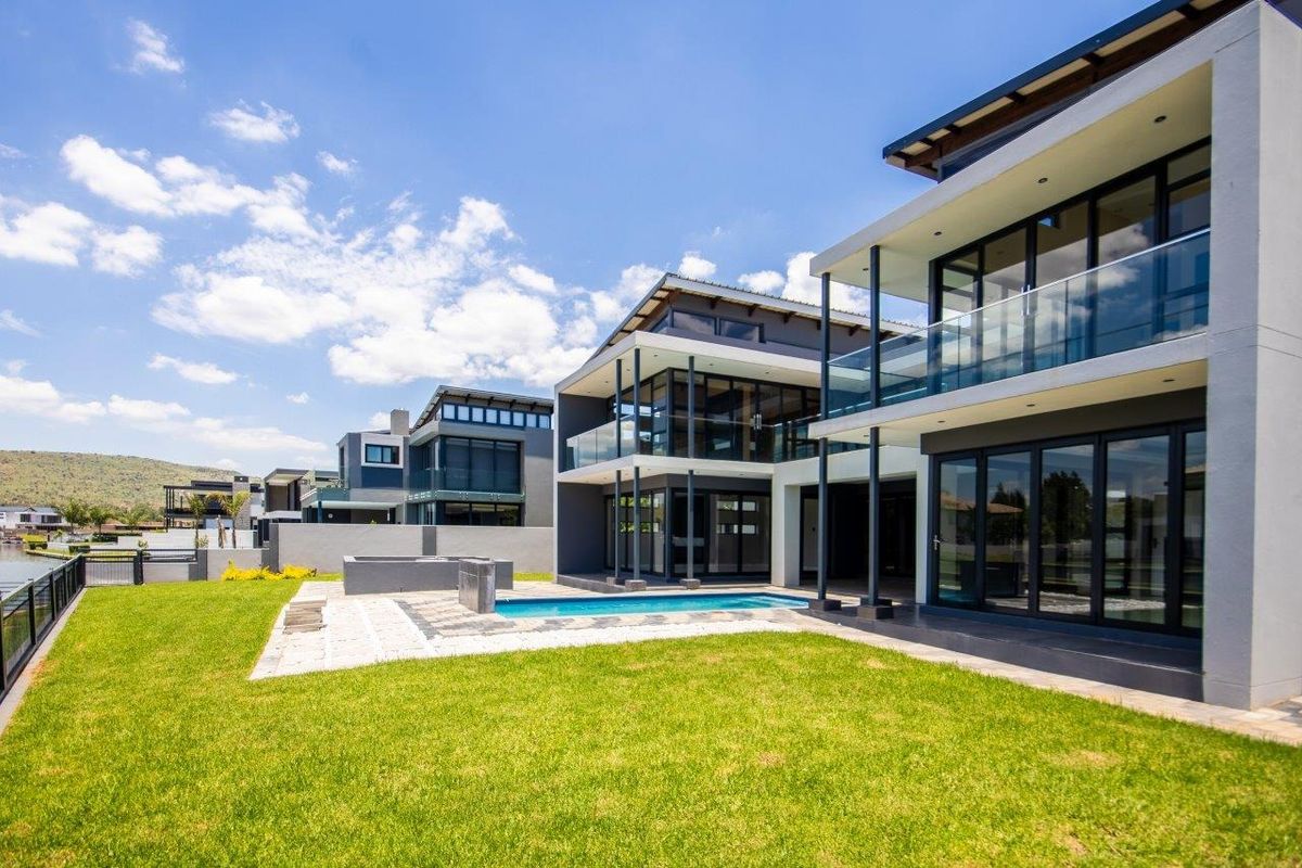Modern multi-story residence featuring expansive glass facades, balconies, a private swimming pool, and a well-maintained lawn in a contemporary estate setting.