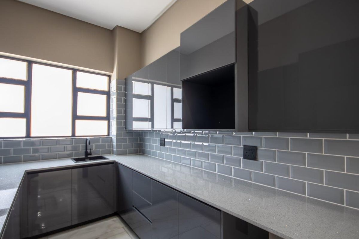 Modern kitchen featuring sleek grey high-gloss cabinetry, stone countertops, and a classic subway tile backsplash with a contemporary black faucet.
