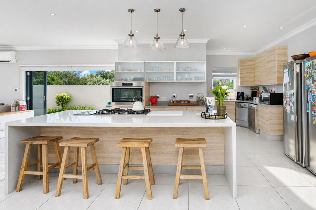 Modern open-plan kitchen featuring a large central island with a built-in gas hob, stone countertops, light wood cabinetry, and integrated stainless steel appliances.