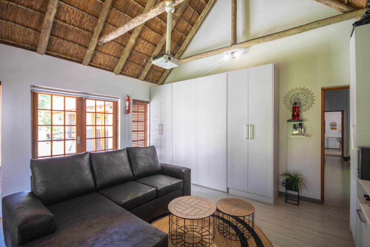 A living room featuring a high vaulted thatched ceiling with exposed timber beams, built-in floor-to-ceiling cabinetry, and wooden-framed glass doors leading outdoors.