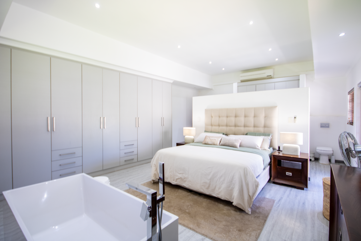 Spacious open-plan bedroom suite featuring extensive built-in cabinetry, a modern freestanding bathtub, and an integrated en-suite bathroom area.