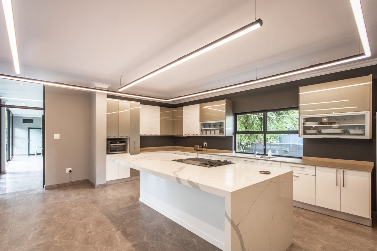 Modern kitchen featuring a large marble-topped island, integrated hob, sleek cabinetry, and contemporary linear pendant lighting.