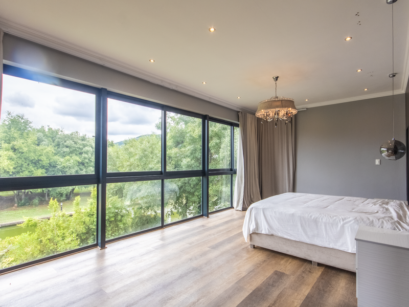 Spacious bedroom featuring floor-to-ceiling windows with scenic garden views, recessed downlighting, and modern wood-look flooring.
