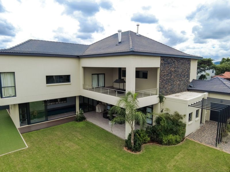Aerial view of a modern two-story house featuring a tiled roof, stone cladding accents, a spacious covered patio, and a well-maintained garden.