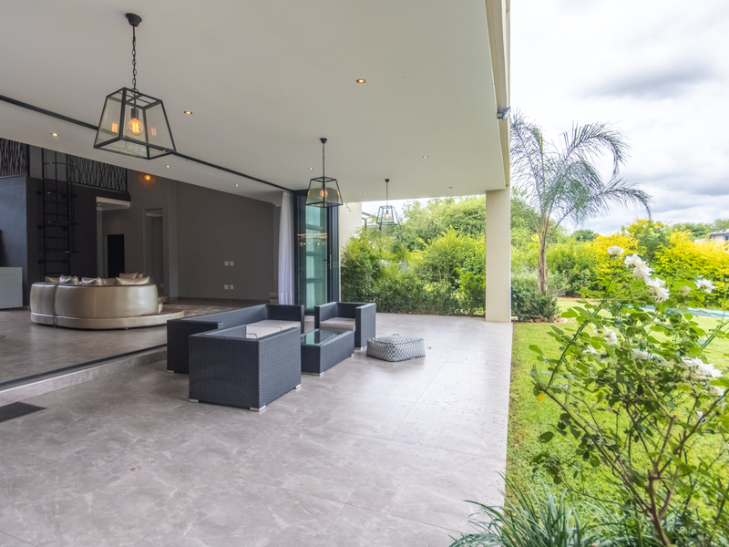 Spacious covered patio featuring large format floor tiles, recessed lighting, and seamless flow into the open-plan living area, overlooking a lush private garden.