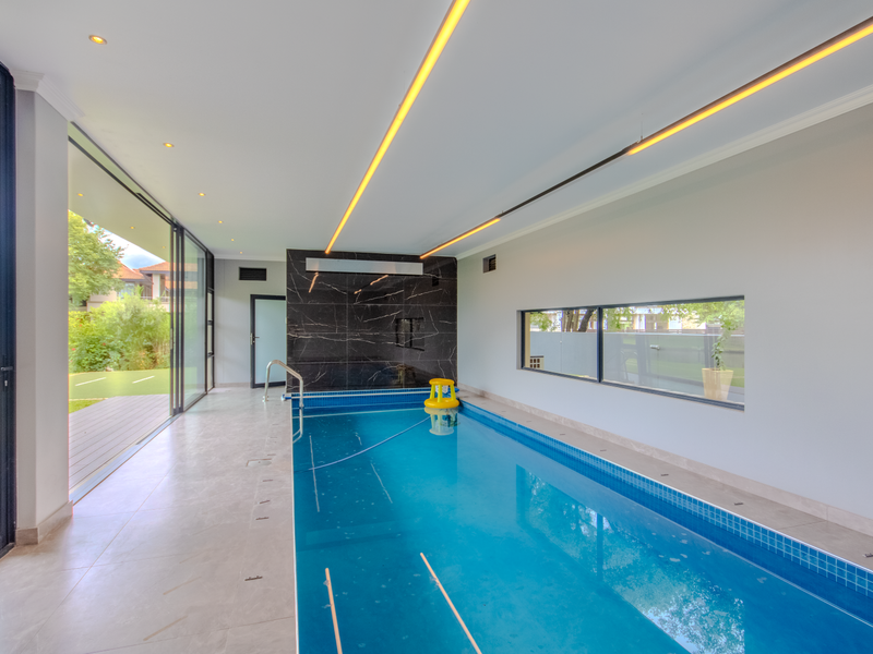 Indoor swimming pool area featuring large sliding glass doors, modern recessed linear lighting, and a dark marble-tiled feature wall.