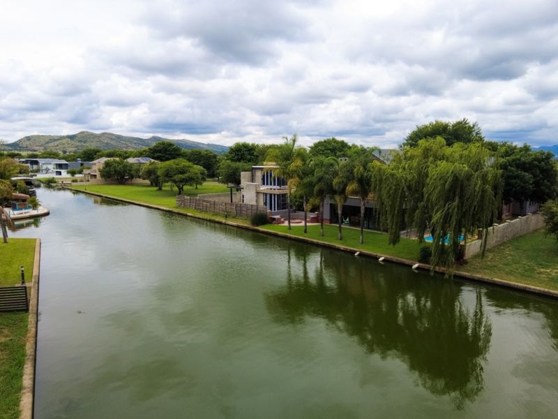 Aerial view of a waterfront property featuring a modern multi-story residence, landscaped garden, and direct canal access in a scenic estate setting.