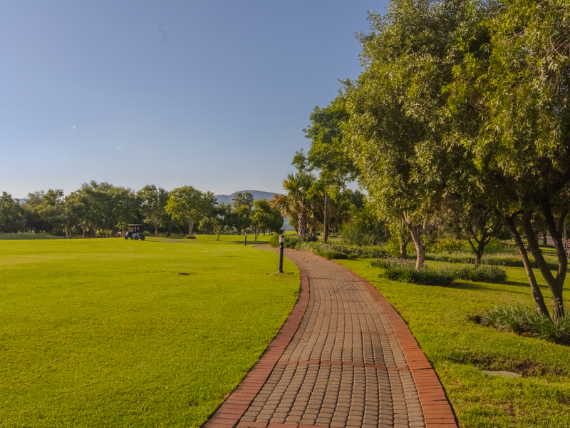 A well-maintained paved walkway winds through a lush, expansive green lawn within a landscaped estate setting.