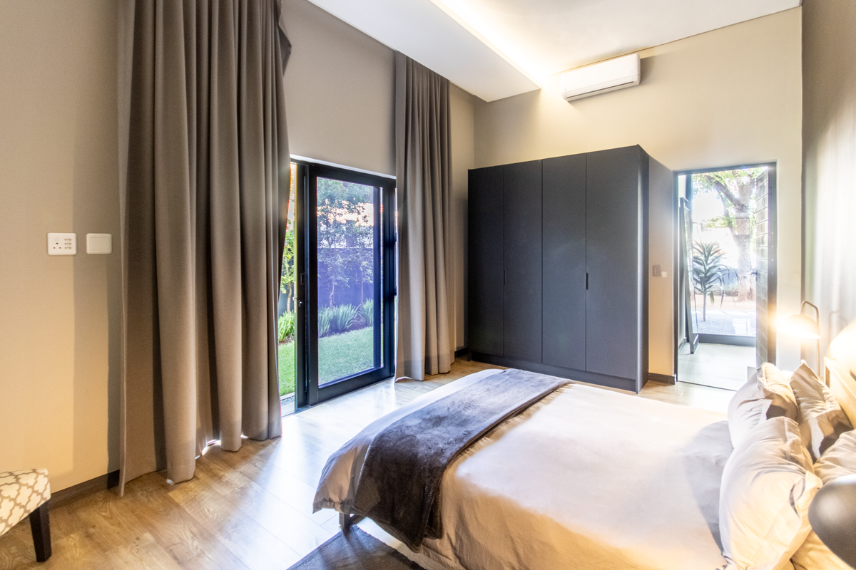 A modern bedroom featuring built-in dark cabinetry, laminate flooring, and direct access to an outdoor garden area through glass sliding doors.