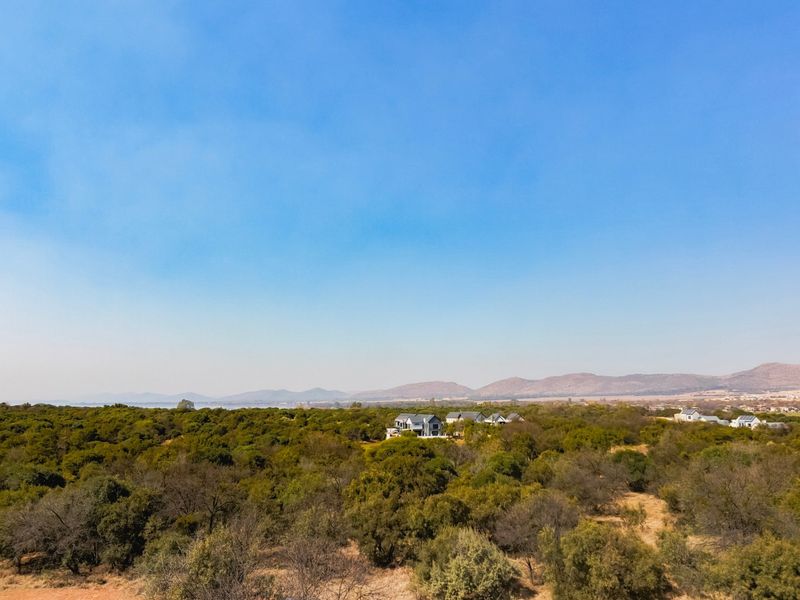 An aerial view of a vast, undeveloped residential land plot featuring natural bushveld vegetation and distant mountain views.