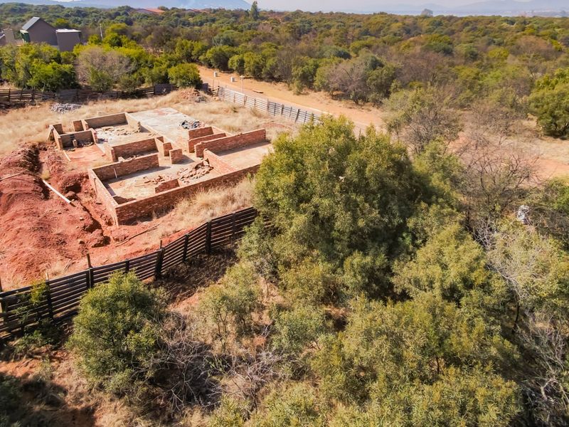 Aerial view of a vacant residential plot featuring an incomplete brick foundation structure surrounded by natural vegetation and perimeter fencing.