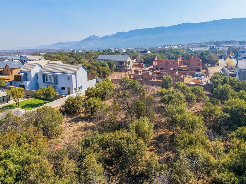 Aerial view of a vacant residential plot surrounded by established homes and natural vegetation in a scenic estate setting.