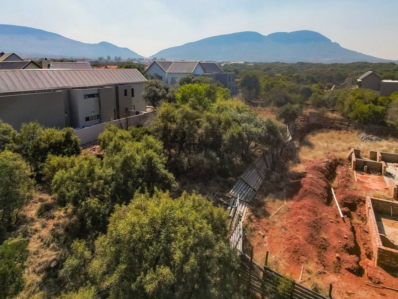 Aerial view of a residential vacant land plot showing ongoing foundation construction, surrounding vegetation, and neighboring properties with mountain views.