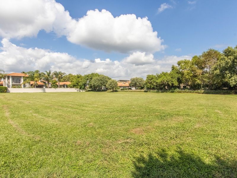 A spacious, well-maintained vacant residential plot featuring a level lawn, mature trees, and established perimeter boundary walls.