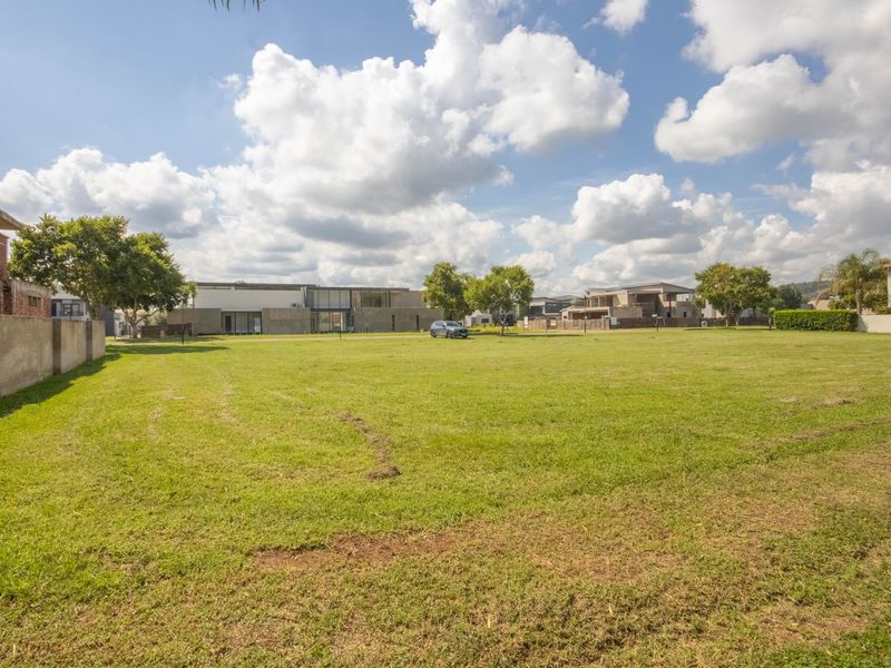 A spacious, level residential vacant land plot featuring a well-maintained lawn and boundary wall, situated in a developed estate setting.