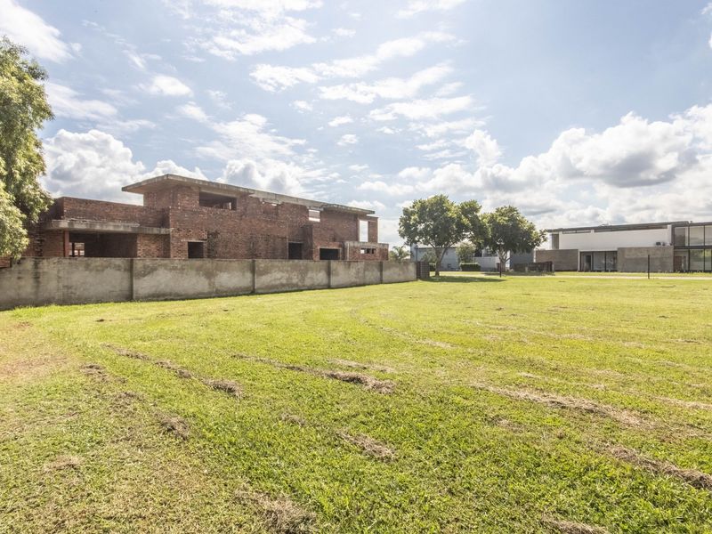 A large vacant residential plot featuring a lawn and an unfinished brick building structure under construction.