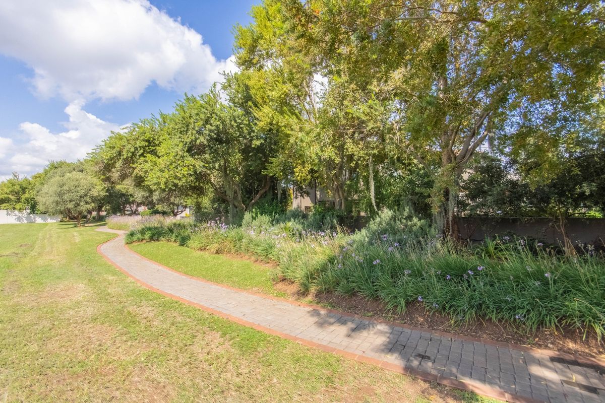 A well-maintained garden area featuring a paved walkway winding through mature trees and established landscaping.
