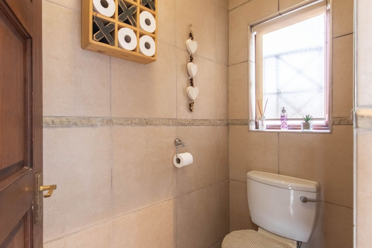 A compact bathroom featuring neutral wall tiles, a standard toilet, and a window providing natural light.