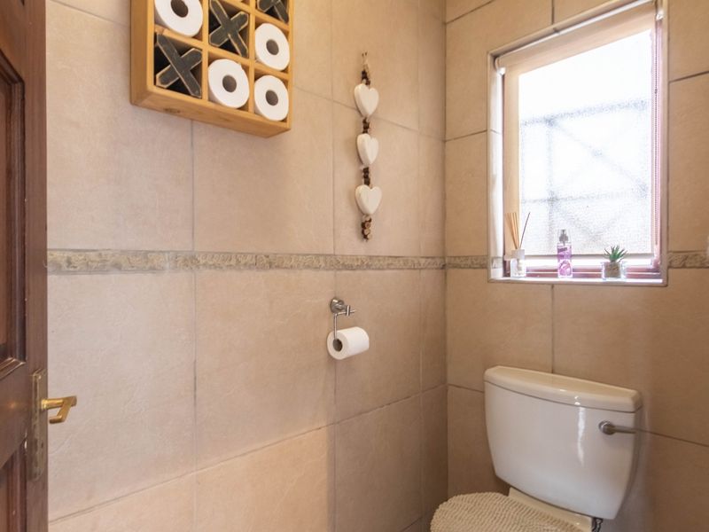 A compact bathroom featuring neutral wall tiles, a standard toilet, and a window providing natural light.