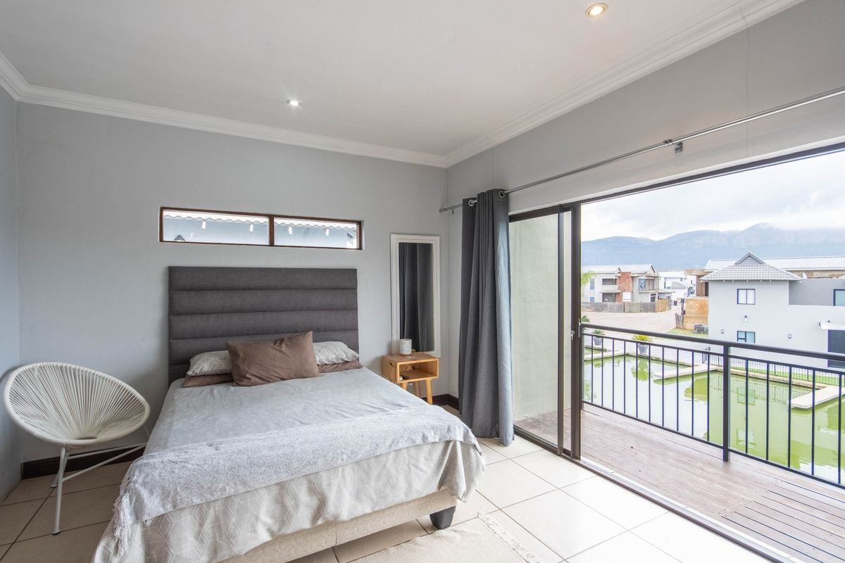 A bright bedroom featuring tiled floors, recessed lighting, and a sliding glass door that opens onto a private balcony with scenic views.