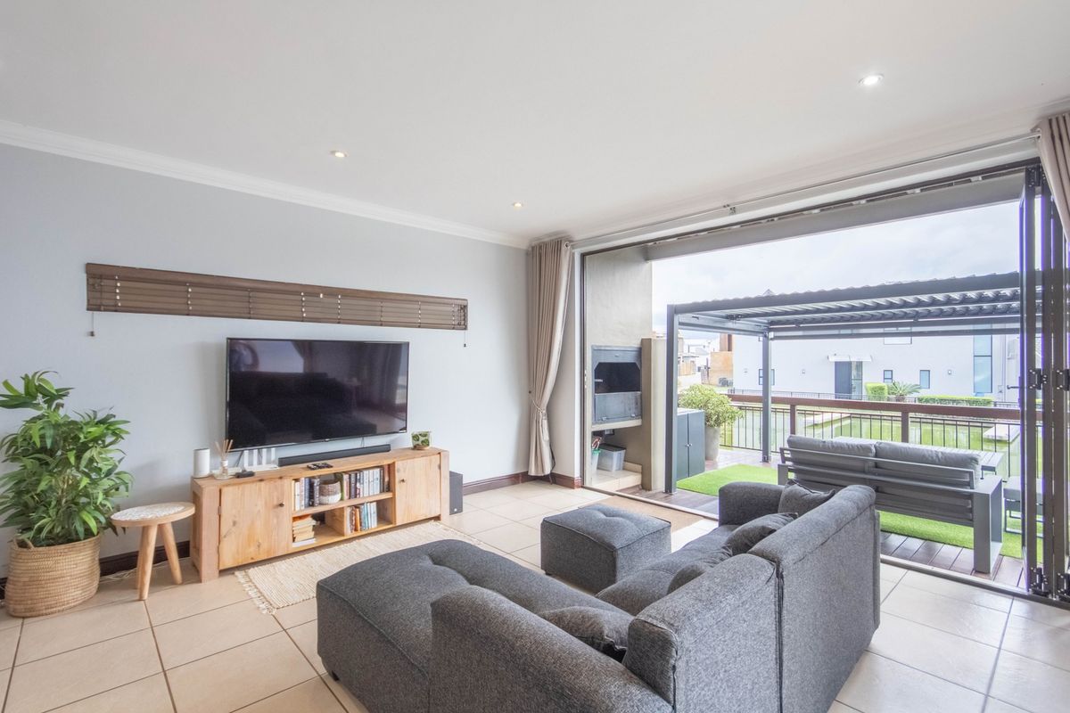 Spacious living room featuring tiled floors and large sliding doors that open onto a covered patio with a built-in braai area.