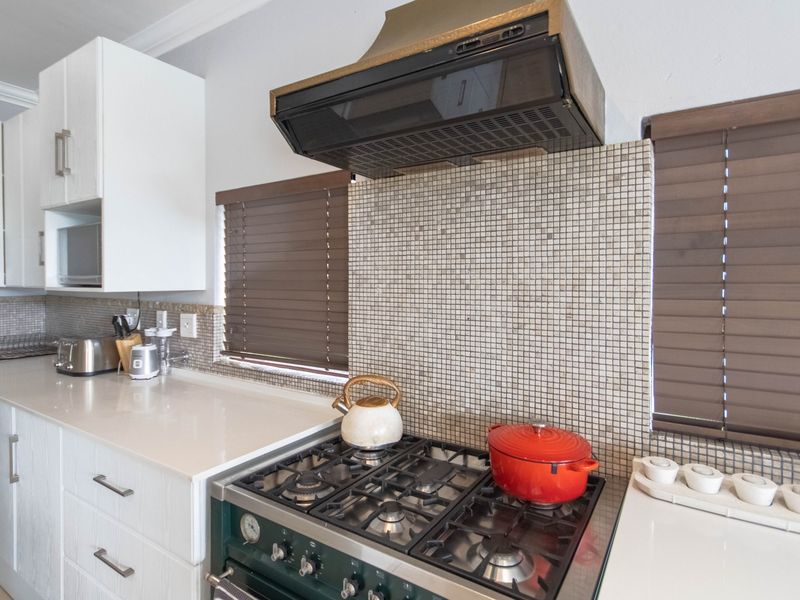 A well-maintained kitchen featuring a gas cooktop, extractor fan, mosaic tile backsplash, and modern white cabinetry with stone countertops.