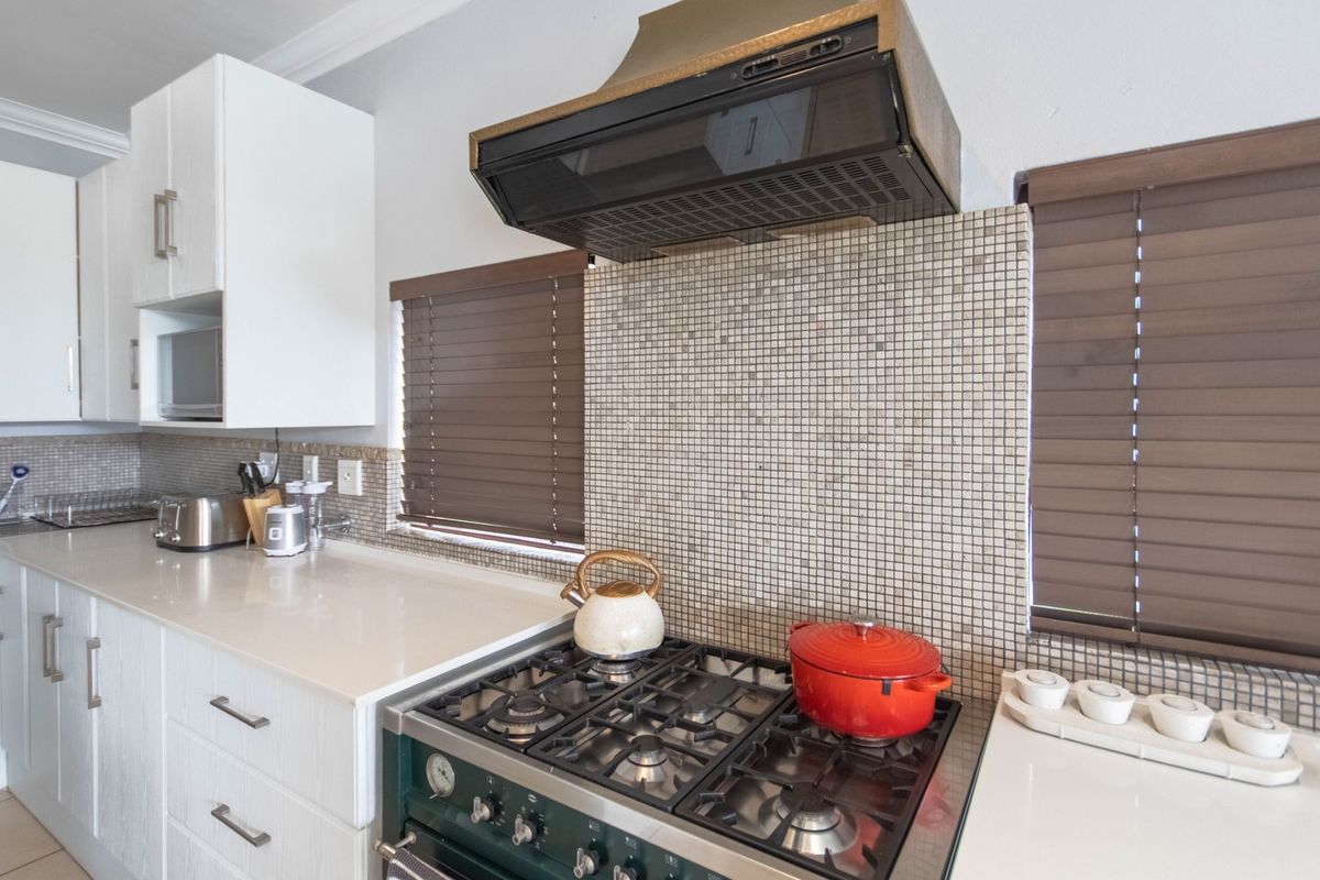 A well-maintained kitchen featuring a gas cooktop, extractor fan, mosaic tile backsplash, and modern white cabinetry with stone countertops.