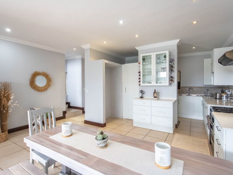 Open-plan kitchen and dining area featuring white cabinetry, tiled flooring, recessed lighting, and a functional layout with a dedicated display cabinet.