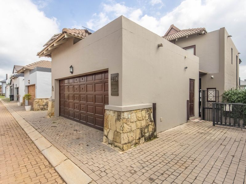 Front exterior view of the property featuring a double garage, stone cladding accents, and a paved driveway in a residential estate setting.