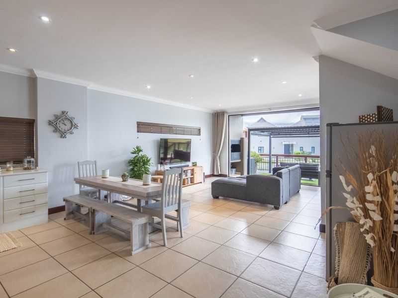 Spacious open-plan living and dining area featuring neutral tiled flooring, recessed lighting, and seamless flow to an outdoor patio through large sliding glass doors.