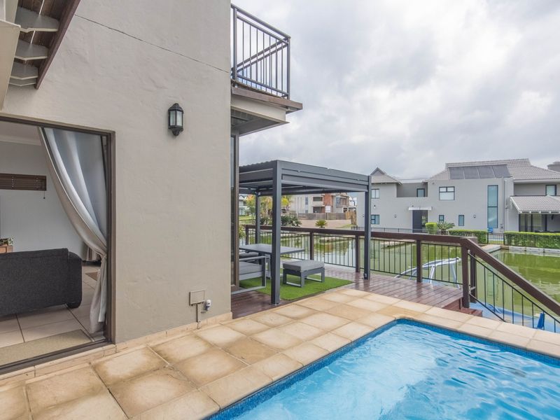Outdoor pool area featuring a wooden deck, metal pergola, and direct access to the living space, overlooking a tranquil water feature.