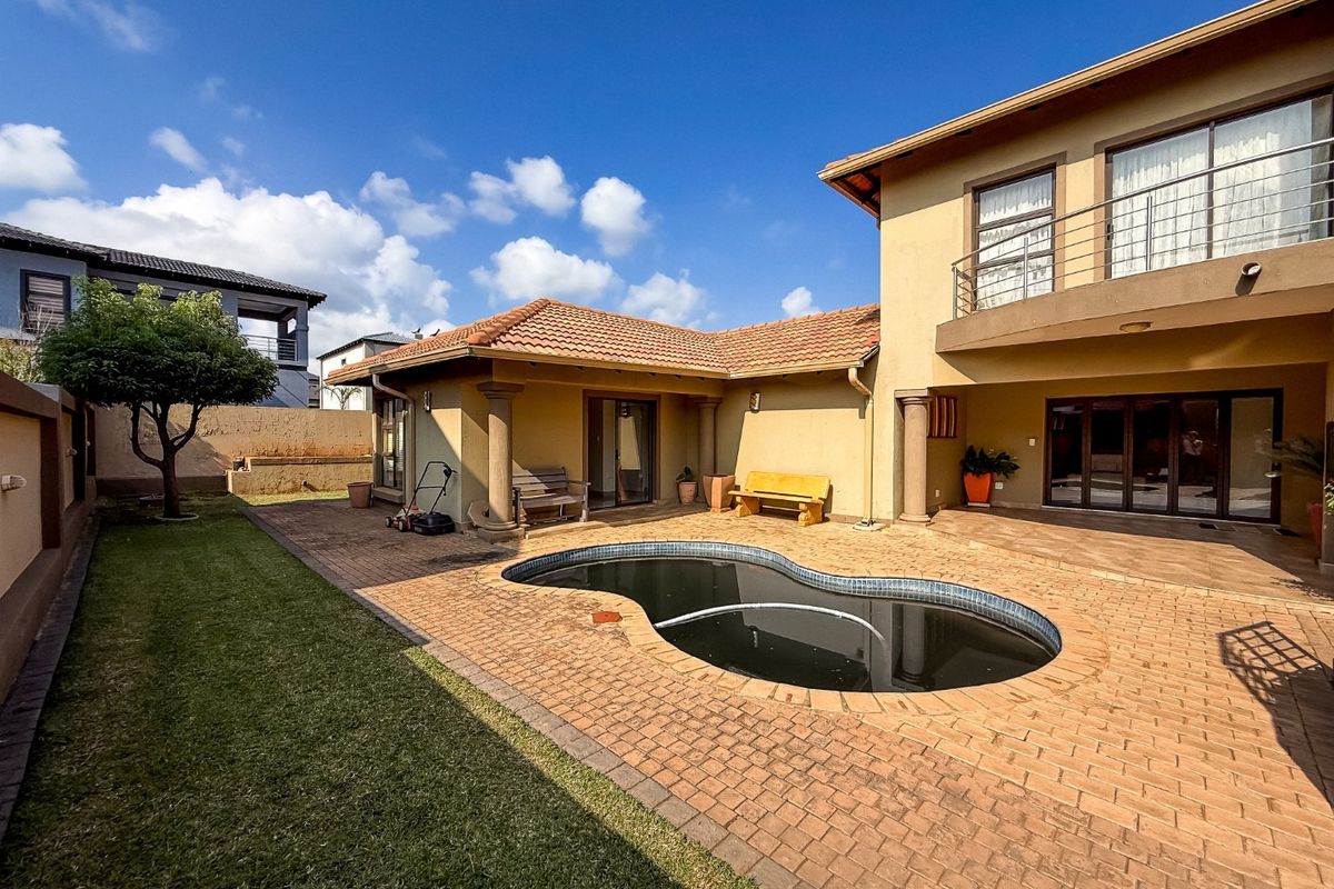 Rear exterior view featuring a kidney-shaped swimming pool, brick paved patio area, and a two-story building facade with a balcony.