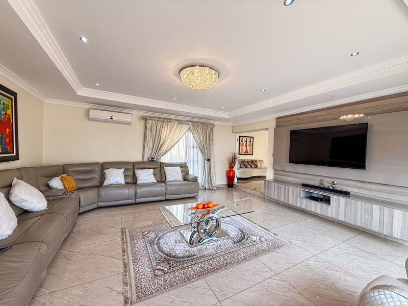 Spacious living room featuring tiled flooring, recessed ceiling lighting, crown molding, and a custom built-in media console.