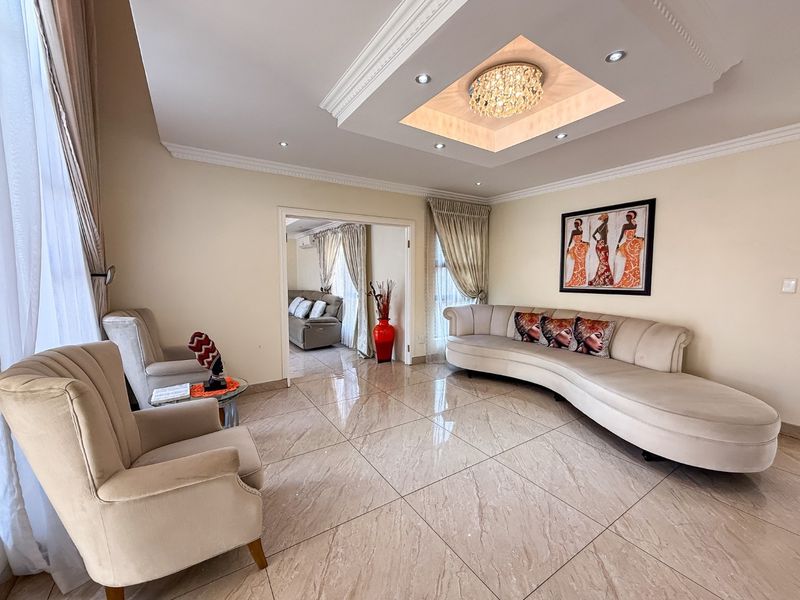 Spacious living room featuring polished porcelain floor tiles, a decorative recessed ceiling with cove lighting, and elegant crown molding.