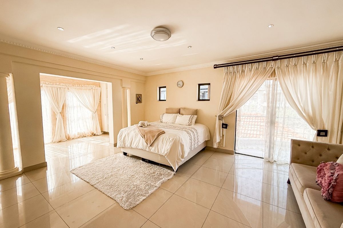Spacious bedroom featuring polished porcelain floor tiles, recessed downlighting, decorative columns, and large sliding glass doors providing access to an outdoor area.