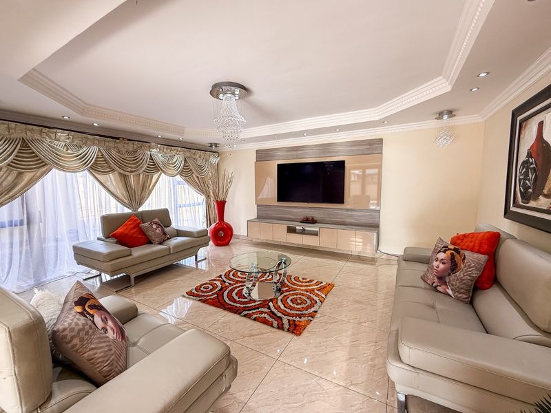 Spacious living room featuring polished tiled flooring, a custom built-in media wall, recessed ceiling with crown molding, and elegant crystal lighting fixtures.