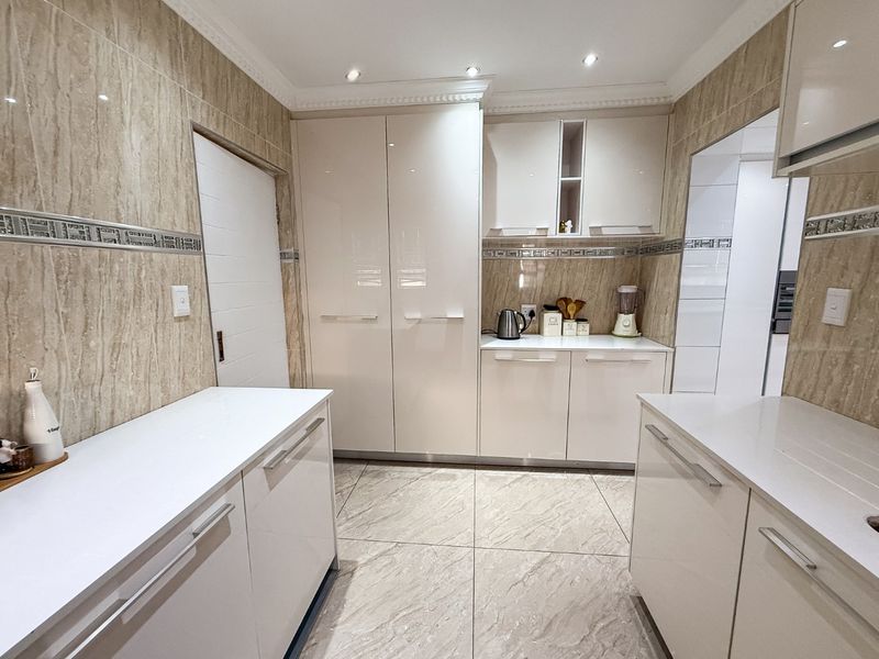 Modern kitchen featuring high-gloss cabinetry, stone countertops, and neutral tiled finishes throughout, offering a clean and functional workspace.