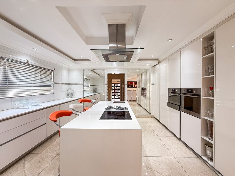Modern, high-end kitchen featuring a central island with integrated cooktop, sleek gloss cabinetry, built-in appliances, and elegant tiled flooring.