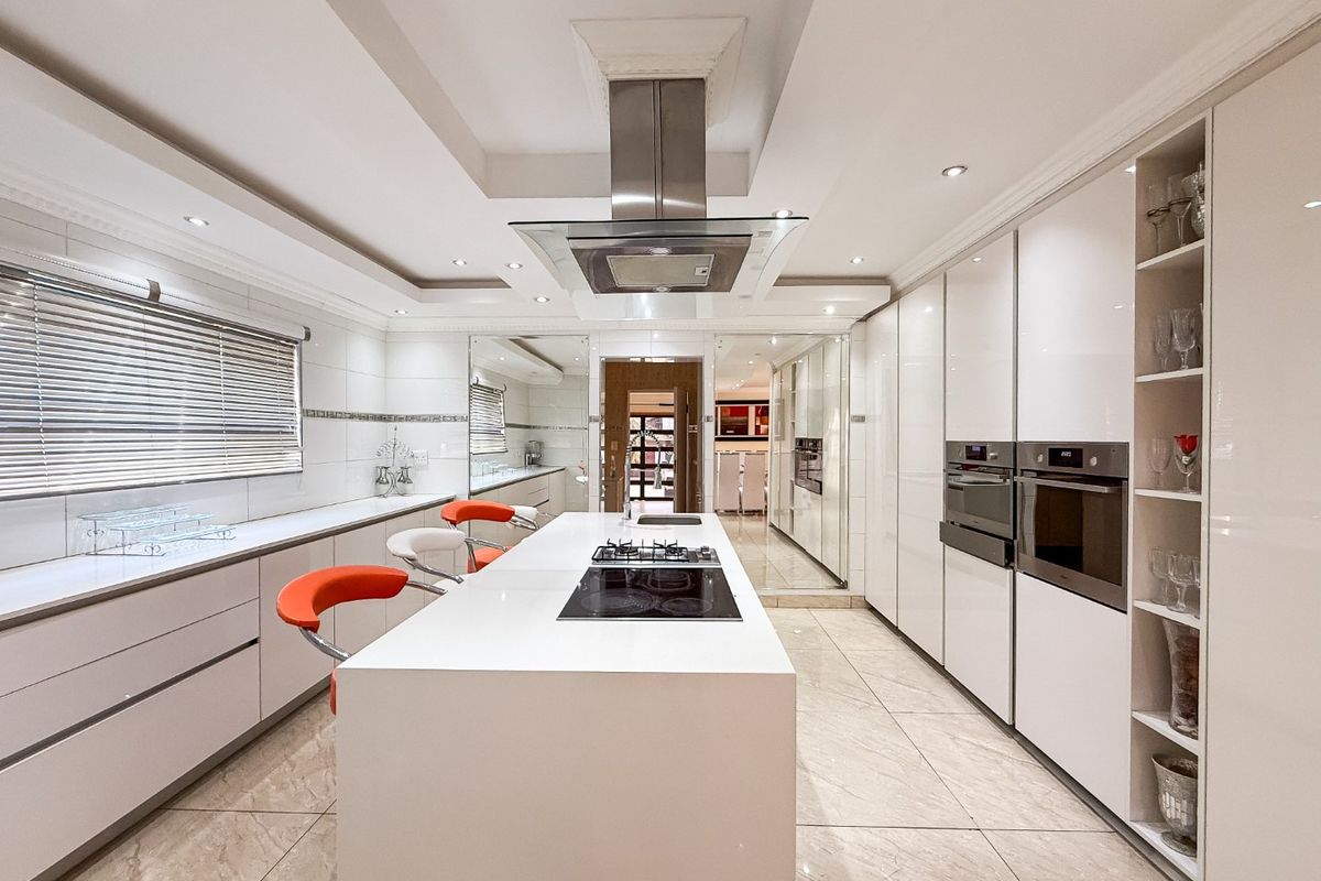 Modern, high-end kitchen featuring a central island with integrated cooktop, sleek gloss cabinetry, built-in appliances, and elegant tiled flooring.