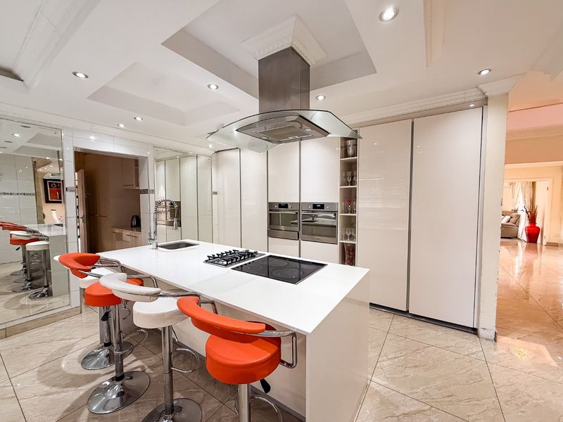 Modern kitchen featuring a central island with integrated gas and electric hobs, built-in ovens, high-gloss cabinetry, and recessed ceiling lighting.
