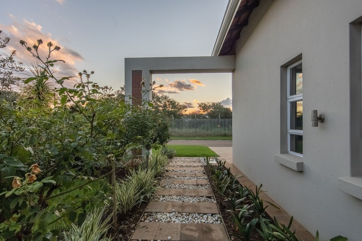 A well-maintained rear garden area featuring a paved walkway, landscaped garden beds, and a modern concrete pergola structure at sunset.