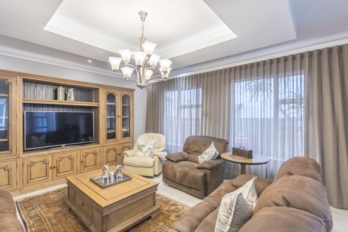 A well-maintained living room featuring custom built-in cabinetry, a sophisticated tray ceiling with recessed lighting, and large windows with floor-to-ceiling curtains.