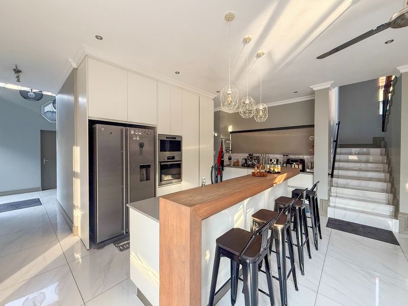 Modern kitchen featuring sleek white cabinetry, a wooden breakfast bar, integrated appliances, and polished tiled flooring, adjacent to a staircase.
