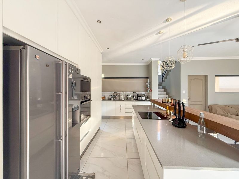 Modern kitchen featuring sleek white cabinetry, stone countertops, a large central island with an integrated hob, and high-quality tiled flooring.
