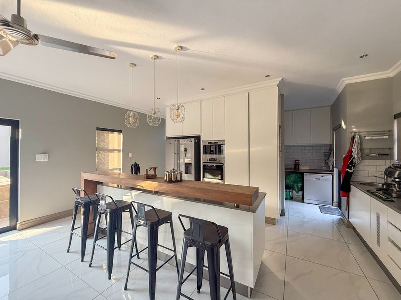 Modern open-plan kitchen featuring a central island with a wooden breakfast bar, sleek white cabinetry, built-in appliances, and polished tiled flooring.